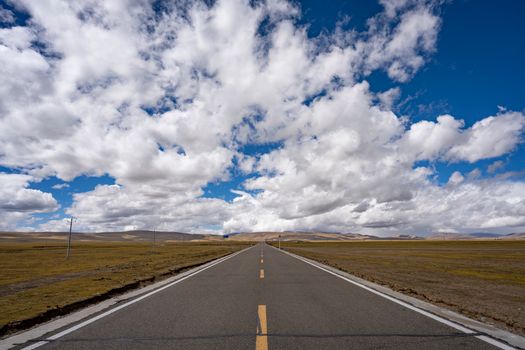 Long open road stretching to horizon under a vast blue sky with fluffy clouds.
