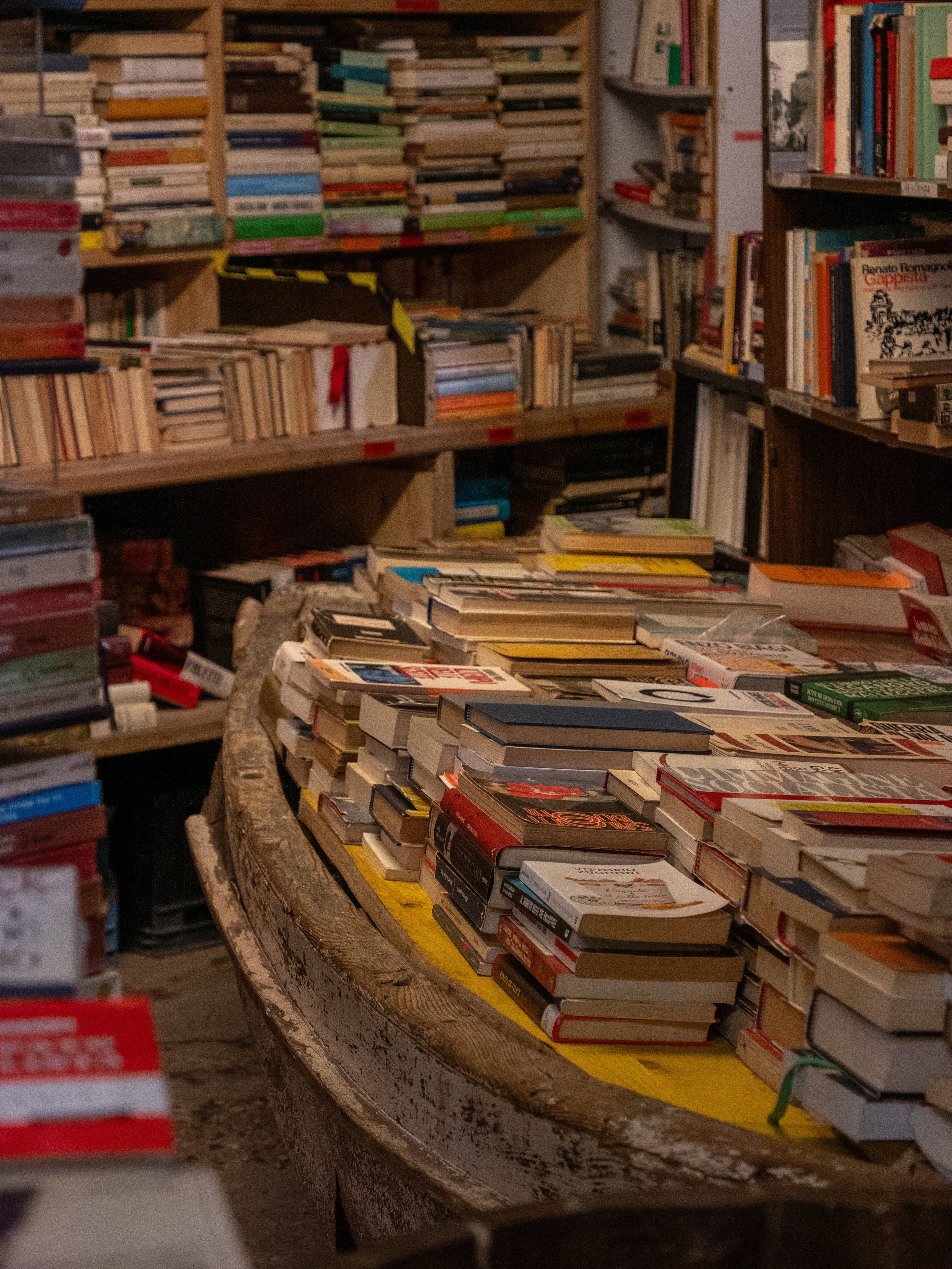 Warm cozy bookstore filled with stacked books on wooden shelving and tables.
