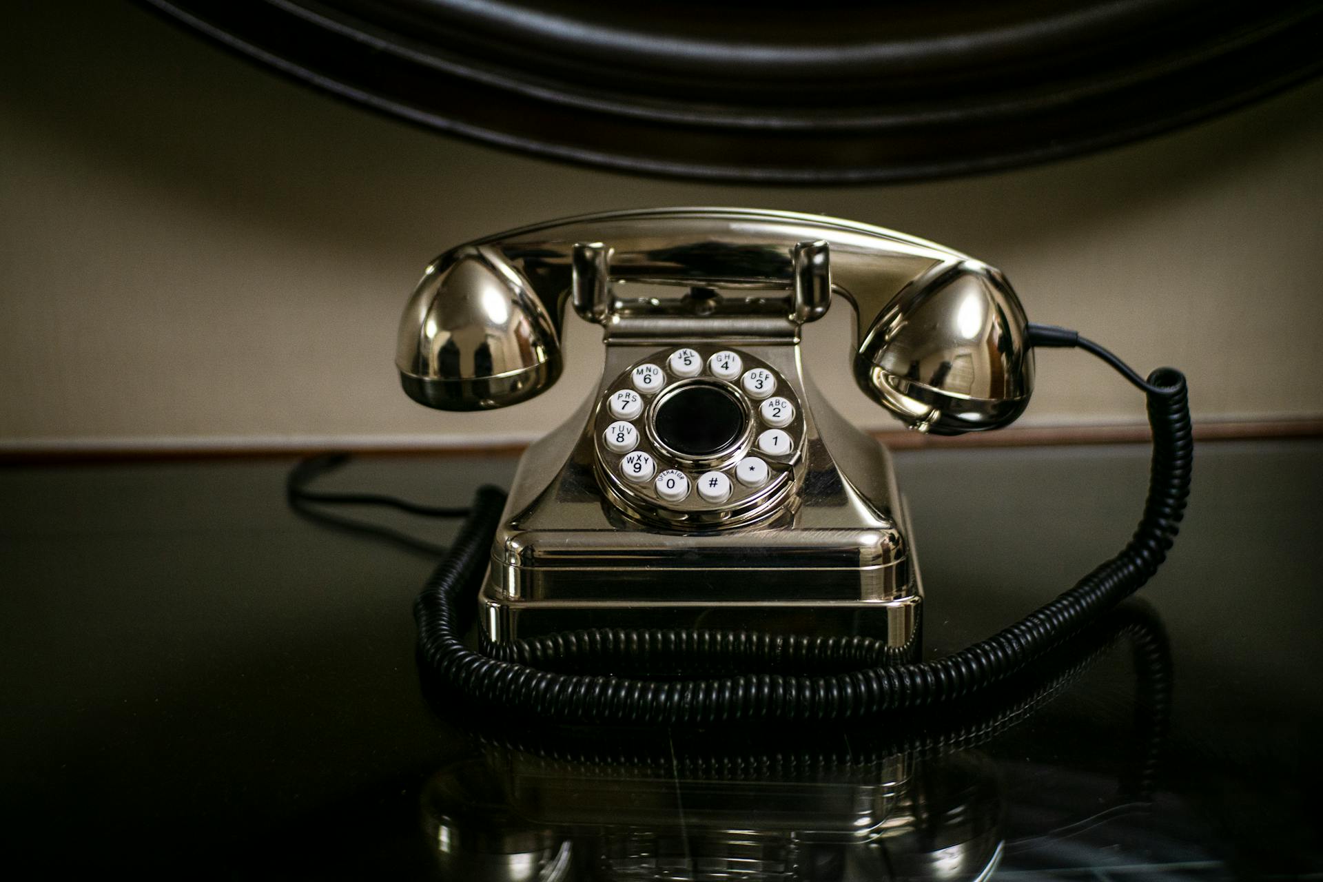 A shiny vintage dial telephone with a coiled cord on a dark reflective surface.