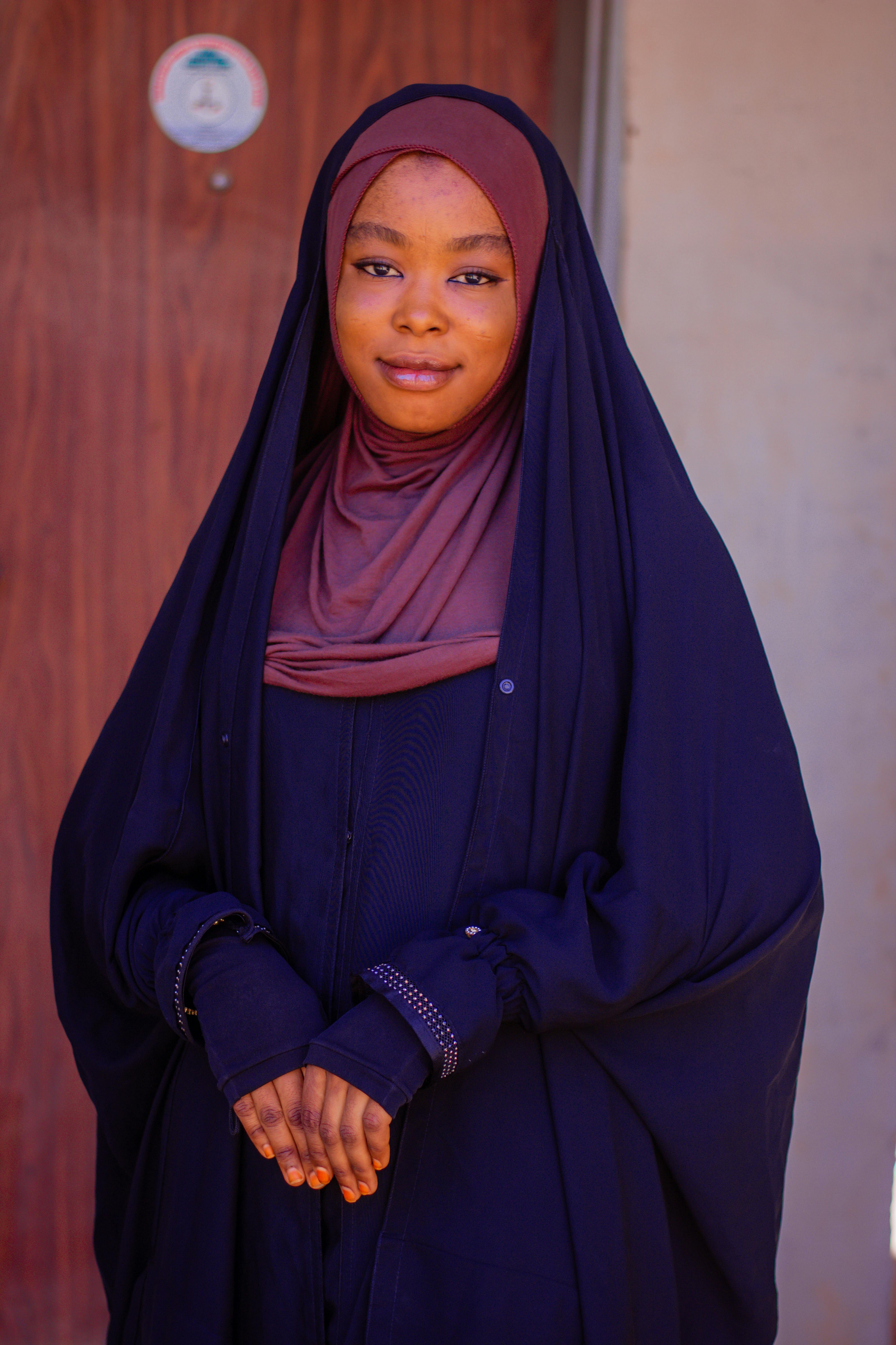 Elegant portrait of a woman in a traditional hijab, standing indoors with a warm expression.