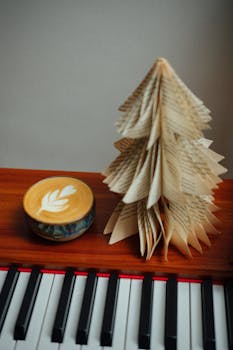 Latte art coffee beside a paper Christmas tree on a piano.