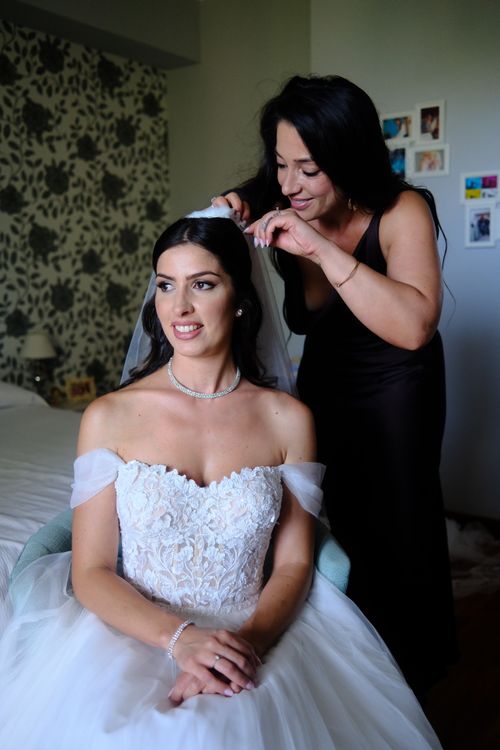 Free A bride prepares for her wedding day as a woman adjusts her veil in a warmly lit room. Stock Photo
