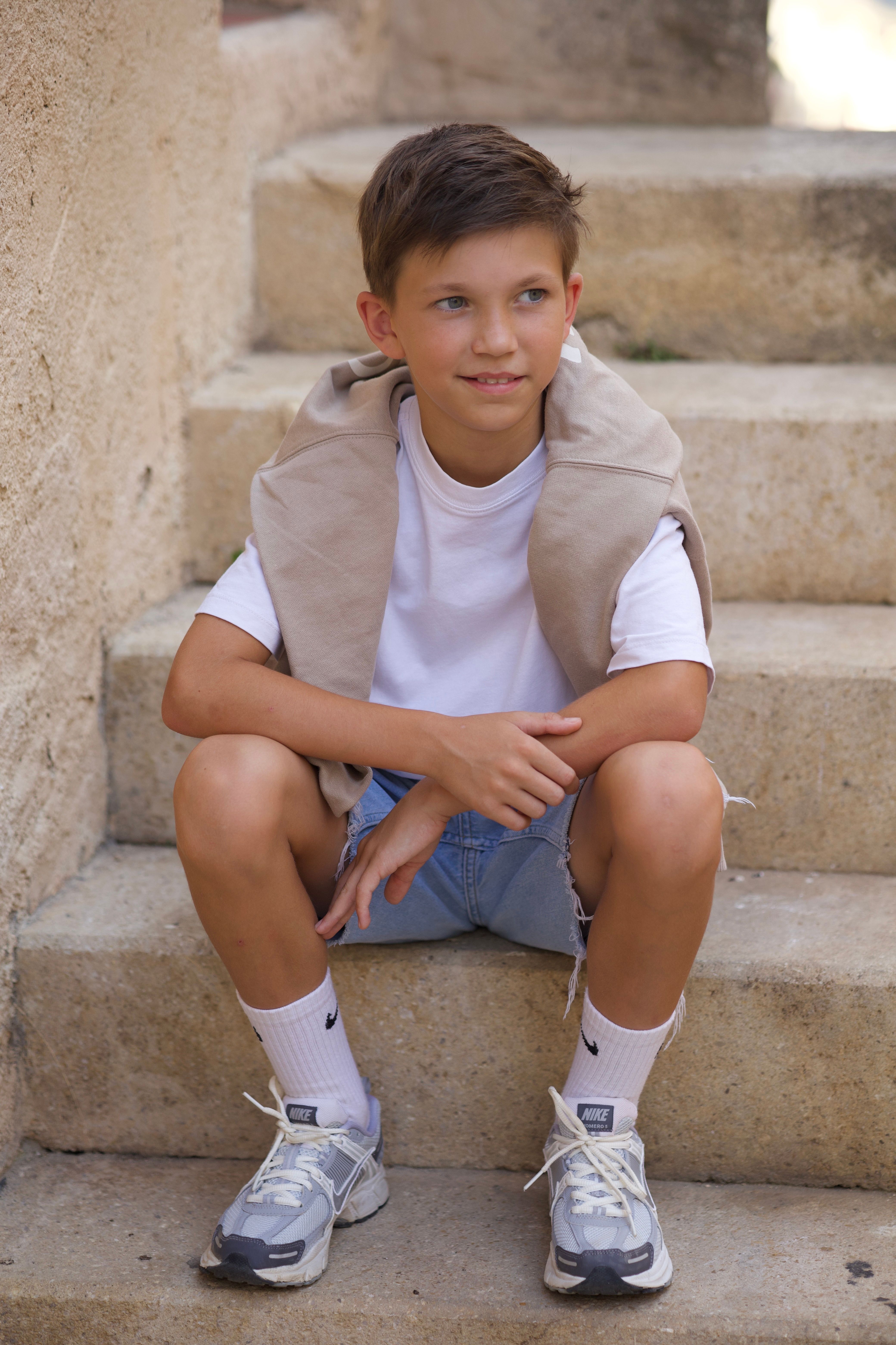 Young boy in casual summer attire sitting on stone stairs, outdoors.