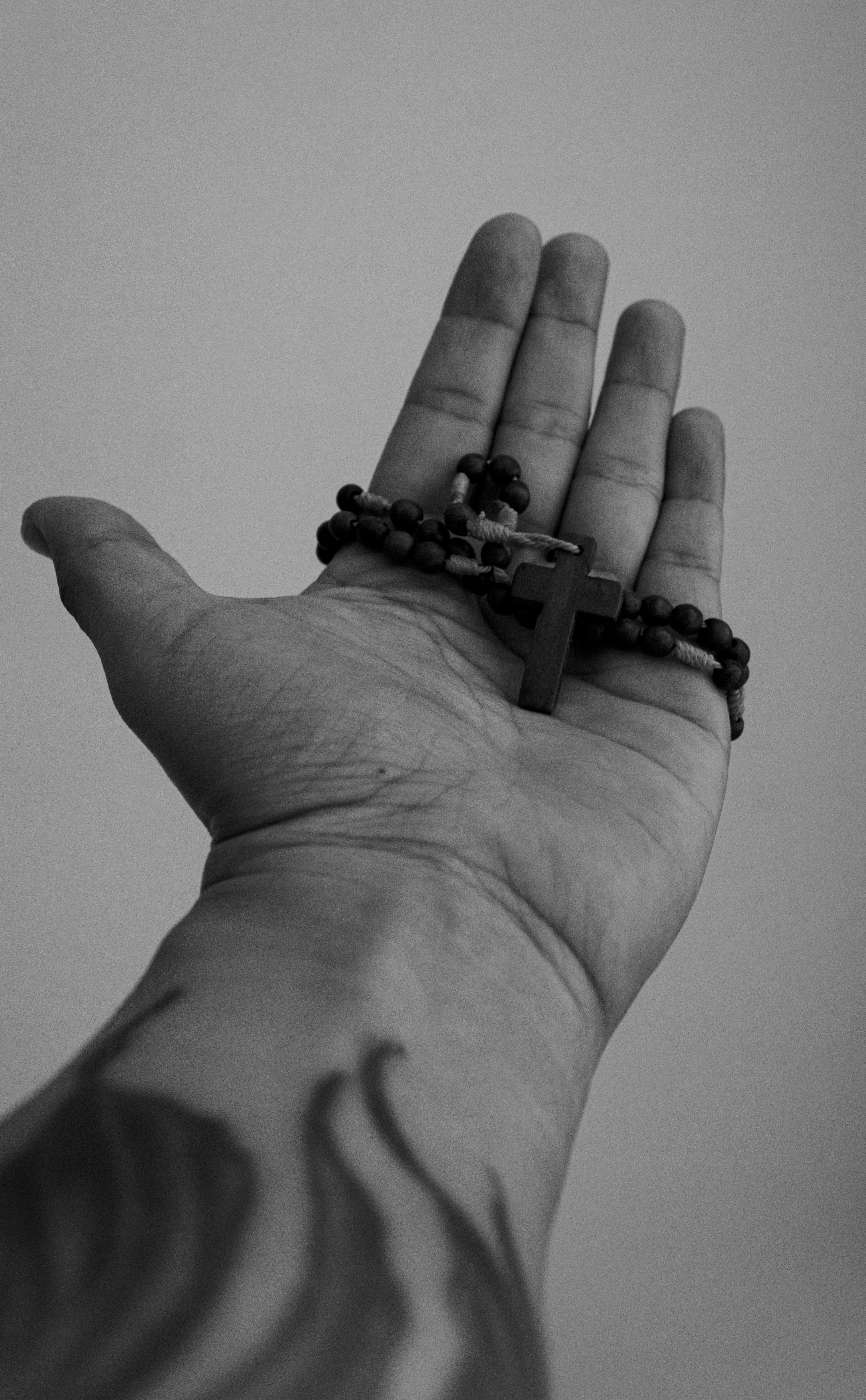 免费 一只纹身手拿着一串带有十字架的念珠的单色照片。 素材图片