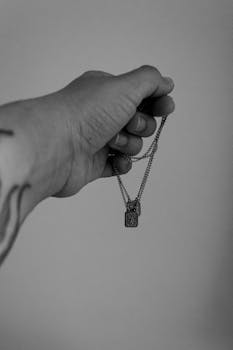 Artistic black and white photo of a hand holding a delicate necklace with a pendant.