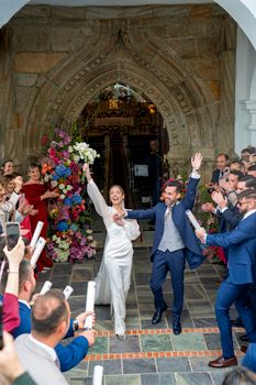 A bride and groom celebrate their wedding with guests at a decorated church entrance.