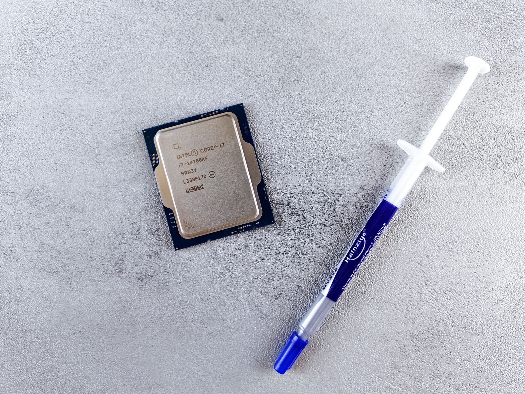 Close-up of an Intel Core i7 processor and syringe of thermal paste on a textured surface.