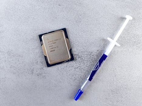 Close-up of an Intel Core i7 processor and syringe of thermal paste on a textured surface.