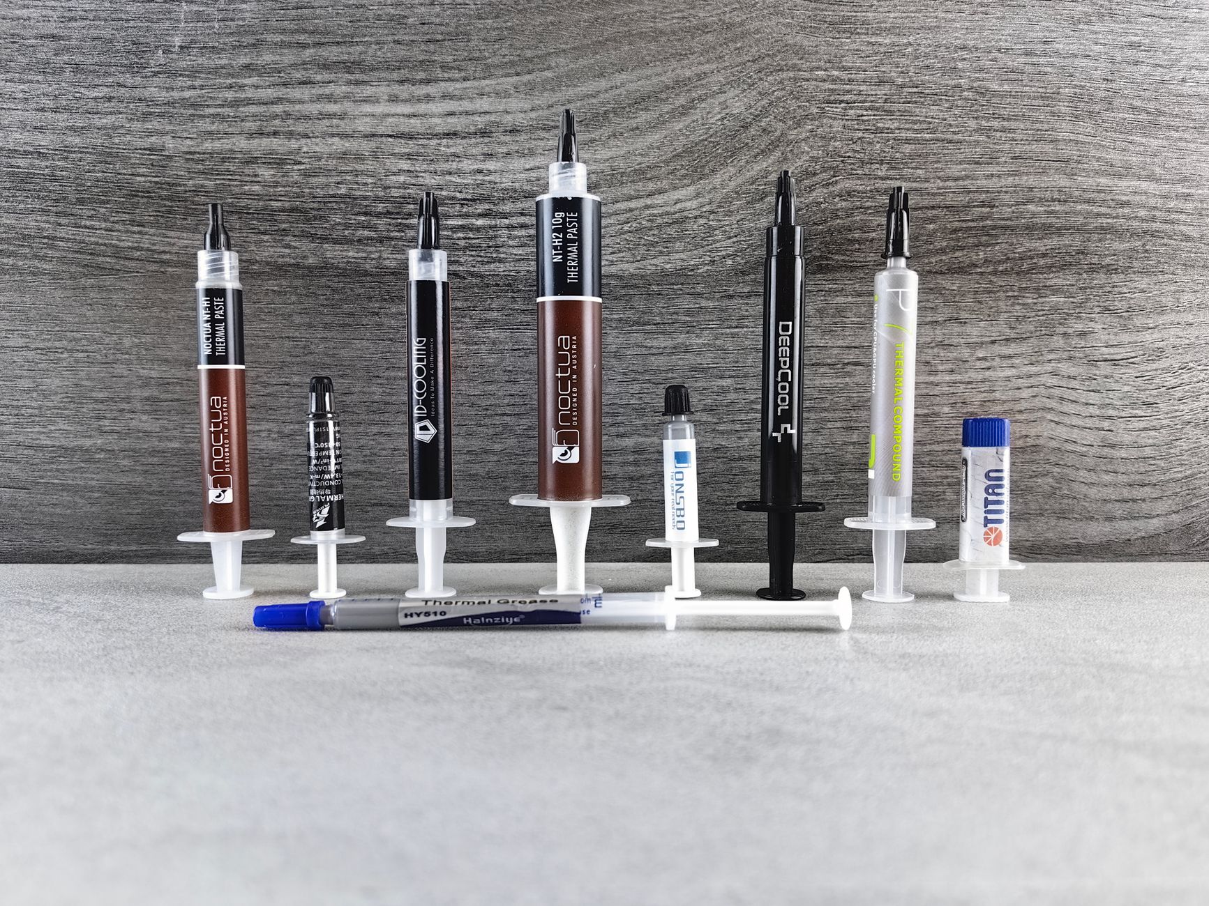 Array of various thermal paste syringes used in computer cooling systems, arranged neatly on a textured surface.