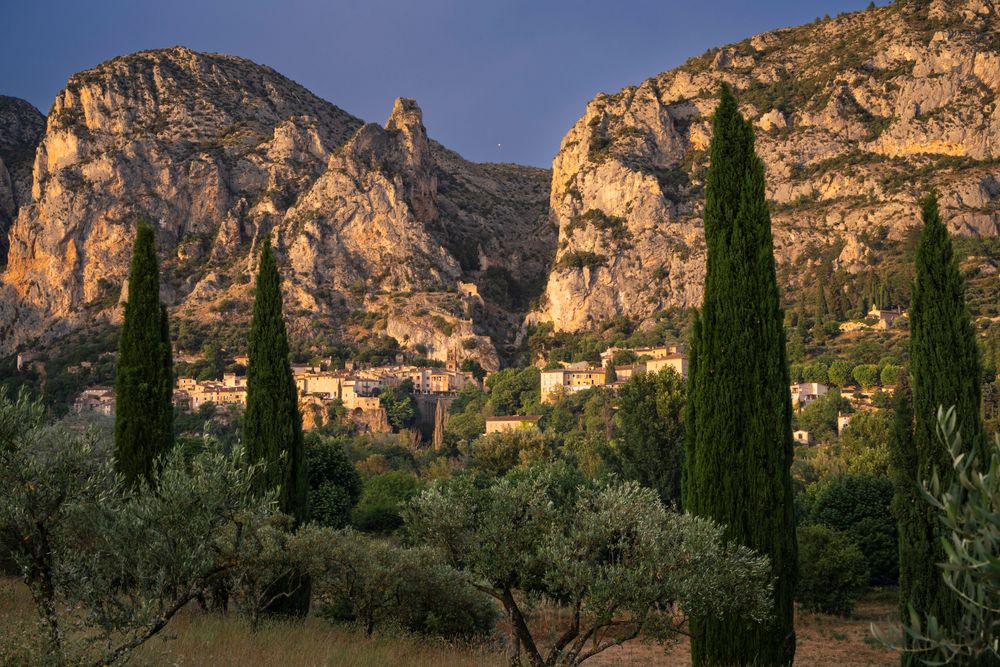 Satul Moustiers-Sainte-Marie între stânci, cu chiparoși, în lumina serii