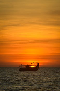 A tranquil scene of a boat silhouetted against a vibrant sunset over calm waters.