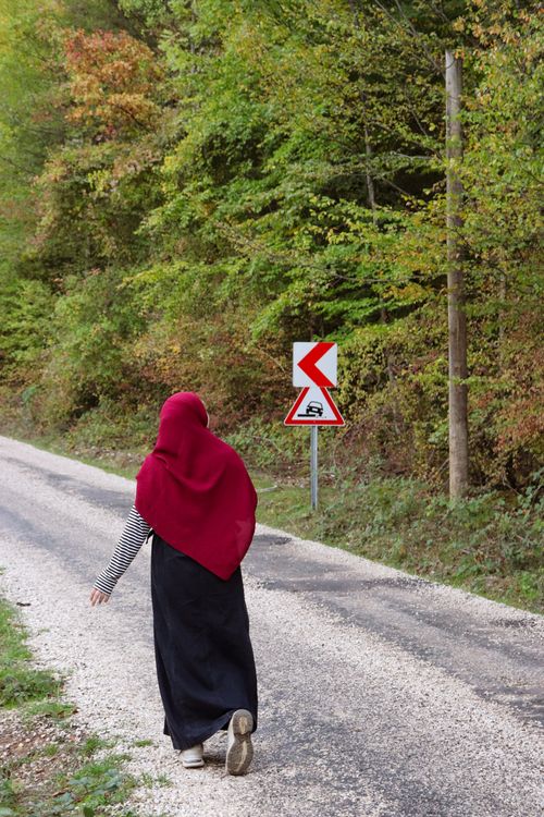 Free A woman in a red hijab walks along a rural road lined with autumn trees. Stock Photo