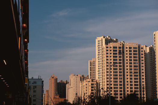 Modern residential skyscrapers in Harbin, China, lit by the warm glow of sunset against a clear sky.