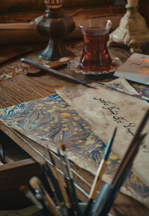 Free Cozy artistic workspace featuring calligraphy, brushes, and a glass of red tea. Stock Photo