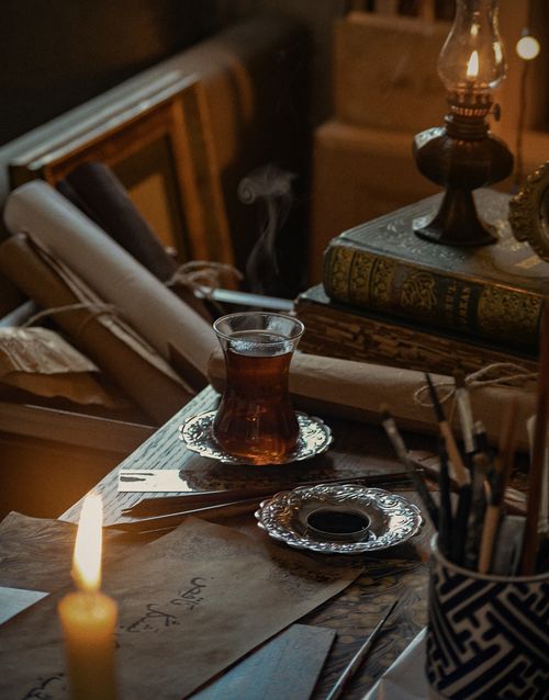 Free Cozy vintage table setup with tea, old books, candlelight. Perfect for warm autumn ambiance. Stock Photo