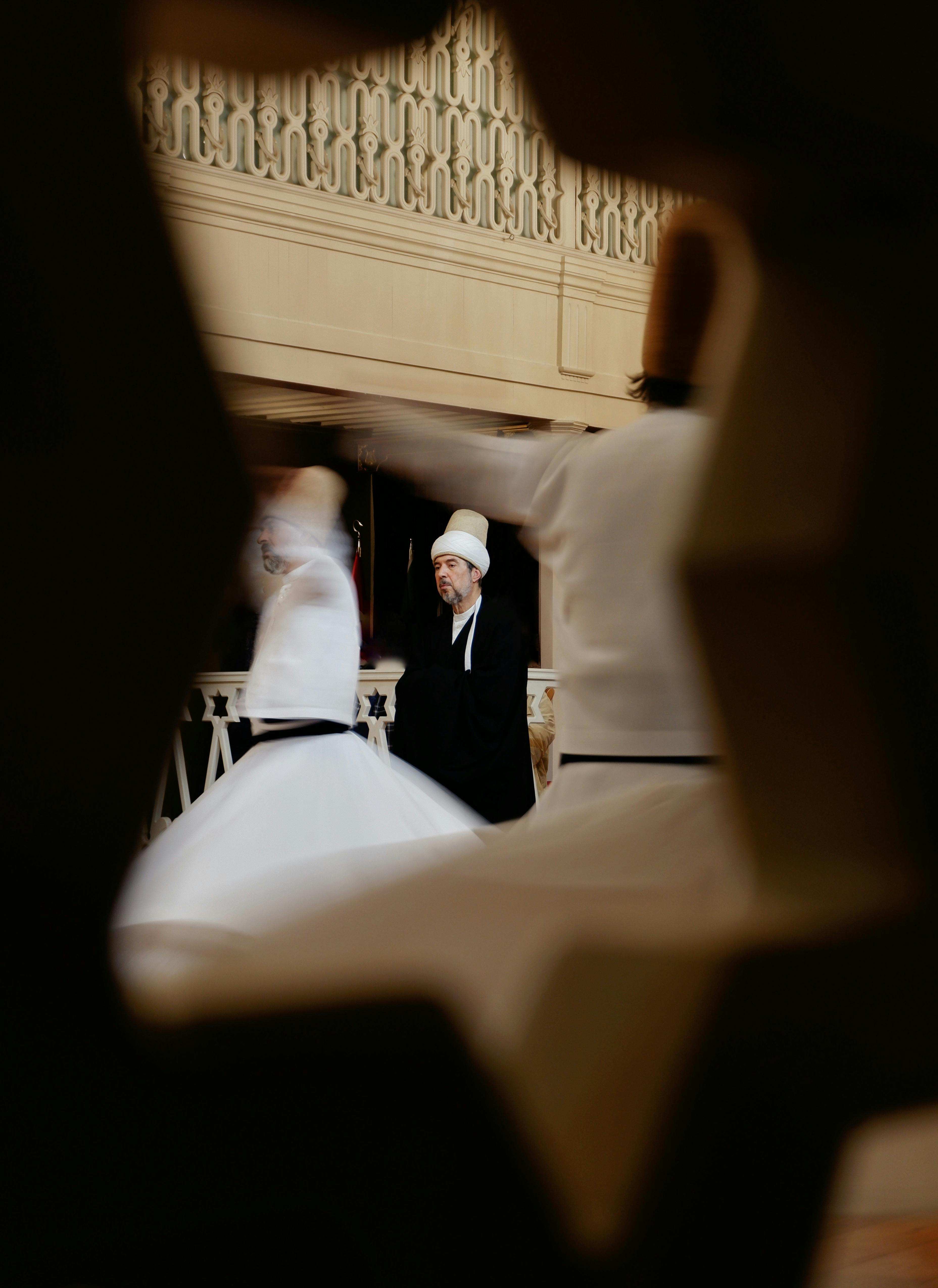 Sufi dancers in motion during a whirling ceremony inside a historic venue.