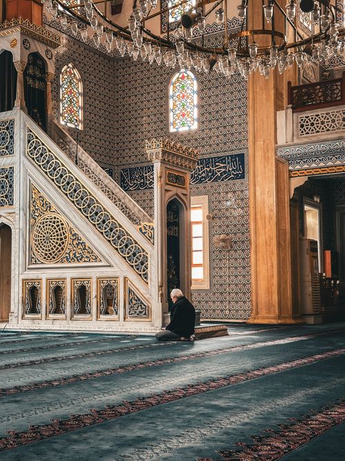 Free An adult man in prayer within a beautifully decorated mosque with intricate stained glass and patterns. Stock Photo