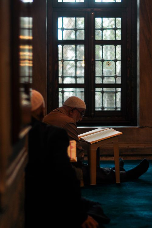 Free An adult man quietly reads a book in a serene mosque setting, illuminated by natural light through a window. Stock Photo