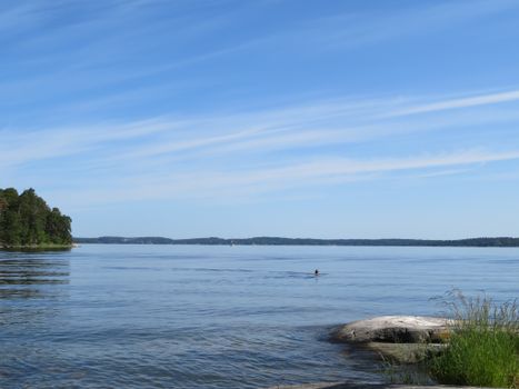 Peaceful lake with blue skies and a lone swimmer, capturing tranquility.