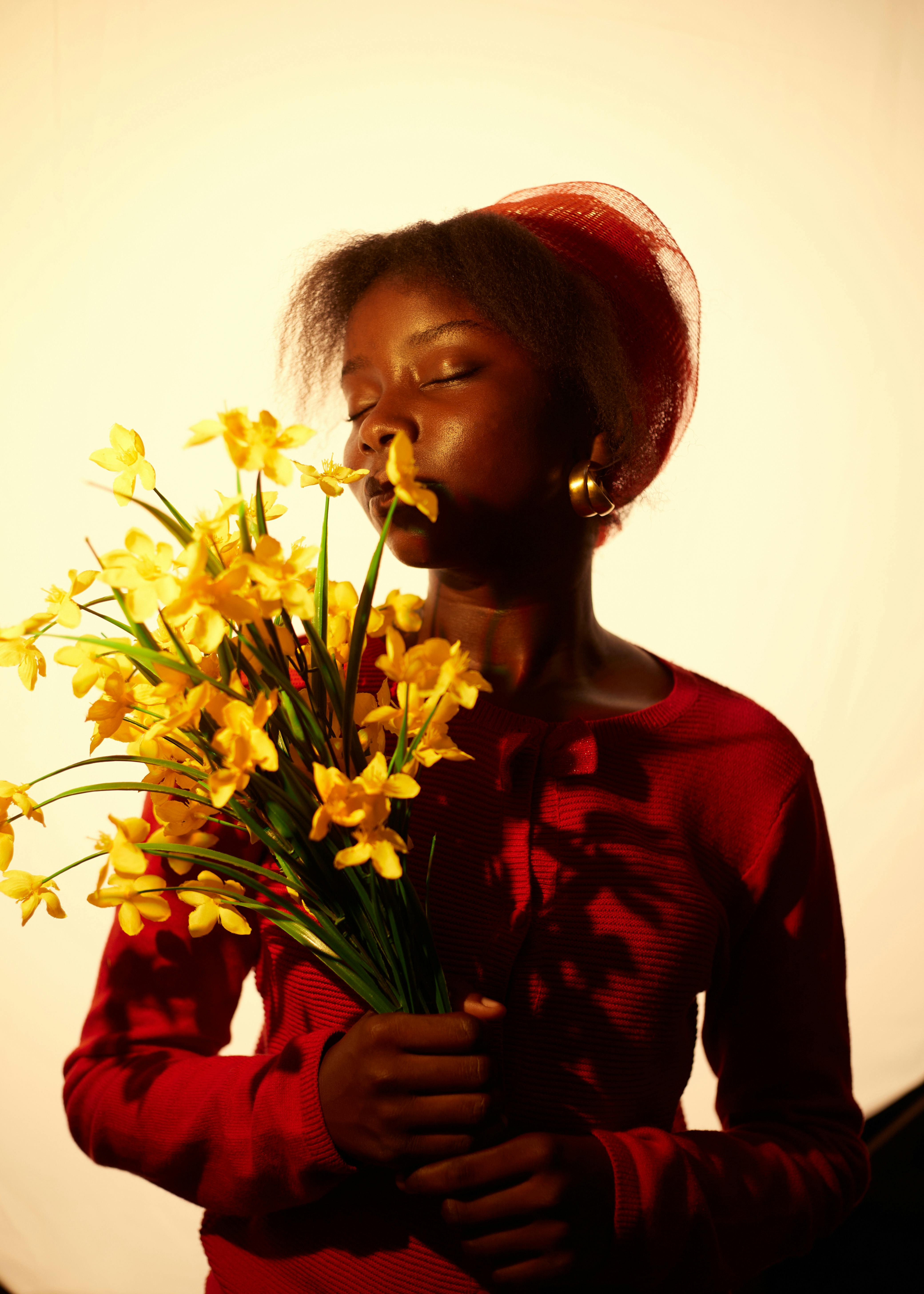 A person in red savoring the scent of yellow flowers in warm, dramatic lighting.