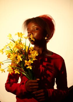 A person in red savoring the scent of yellow flowers in warm, dramatic lighting.
