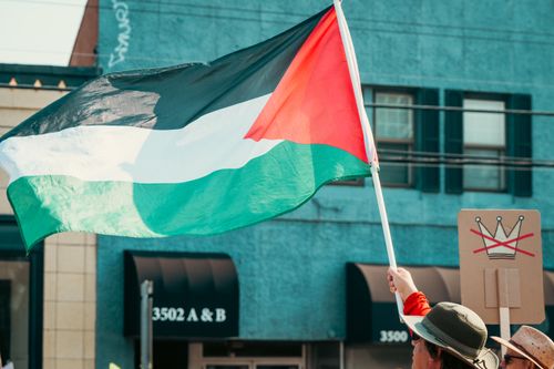 Free Demonstrator holding a Palestinian flag at a protest in an urban area. Stock Photo
