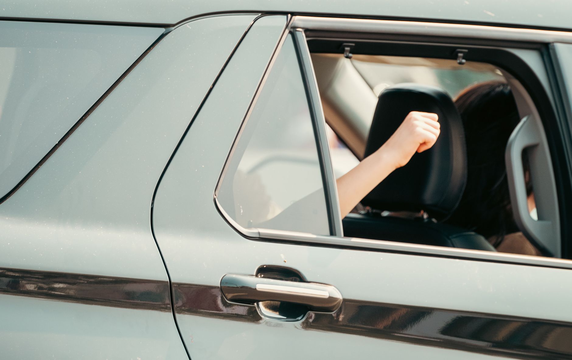A person raises their arm out of a moving car window, expressing joy and freedom.