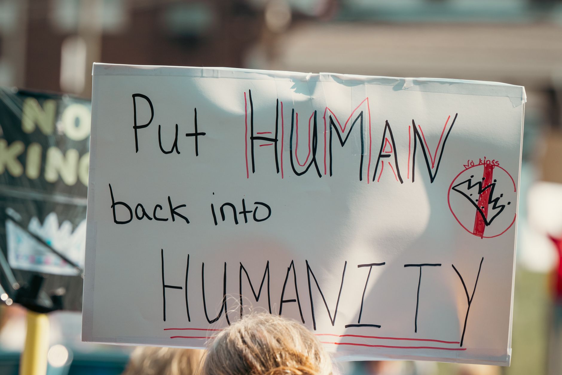 A protest sign with the message 'Put Human back into Humanity' during a daylight rally.