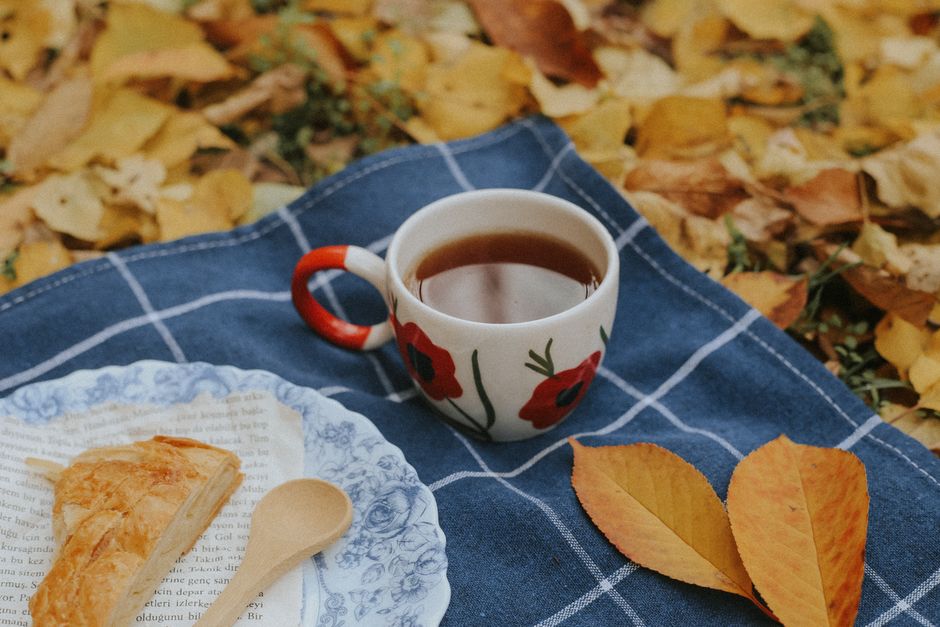 Cozy autumn picnic scene with tea and pastry on a blanket surrounded by fall leaves.