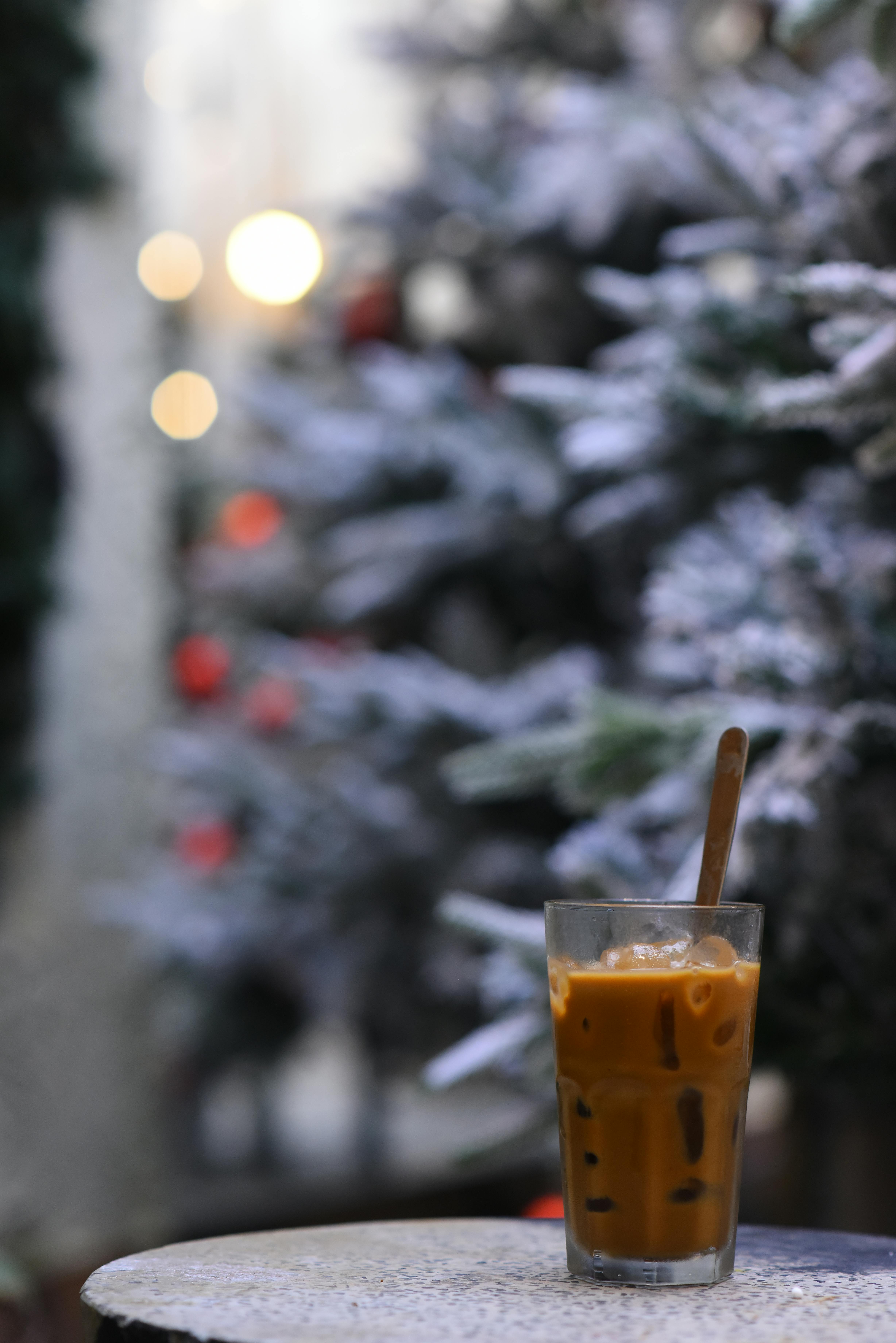 A glass of iced coffee on a table, with a frosty winter background and festive lights.