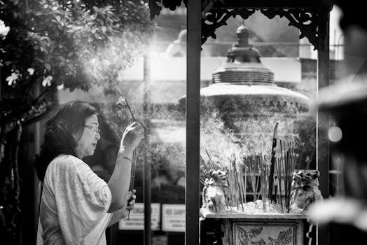 A woman prays with incense sticks, creating smoke clouds around a temple altar outdoors.