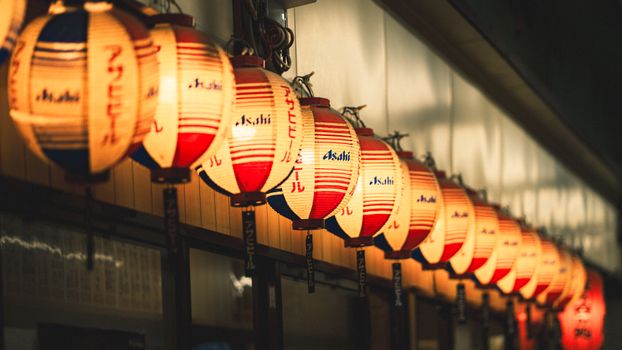 A row of traditional Japanese lanterns hanging indoors, creating a warm and vibrant atmosphere.