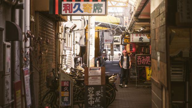 A vibrant Japanese alleyway scene featuring bicycles, a man in a cap, and bustling small shops.