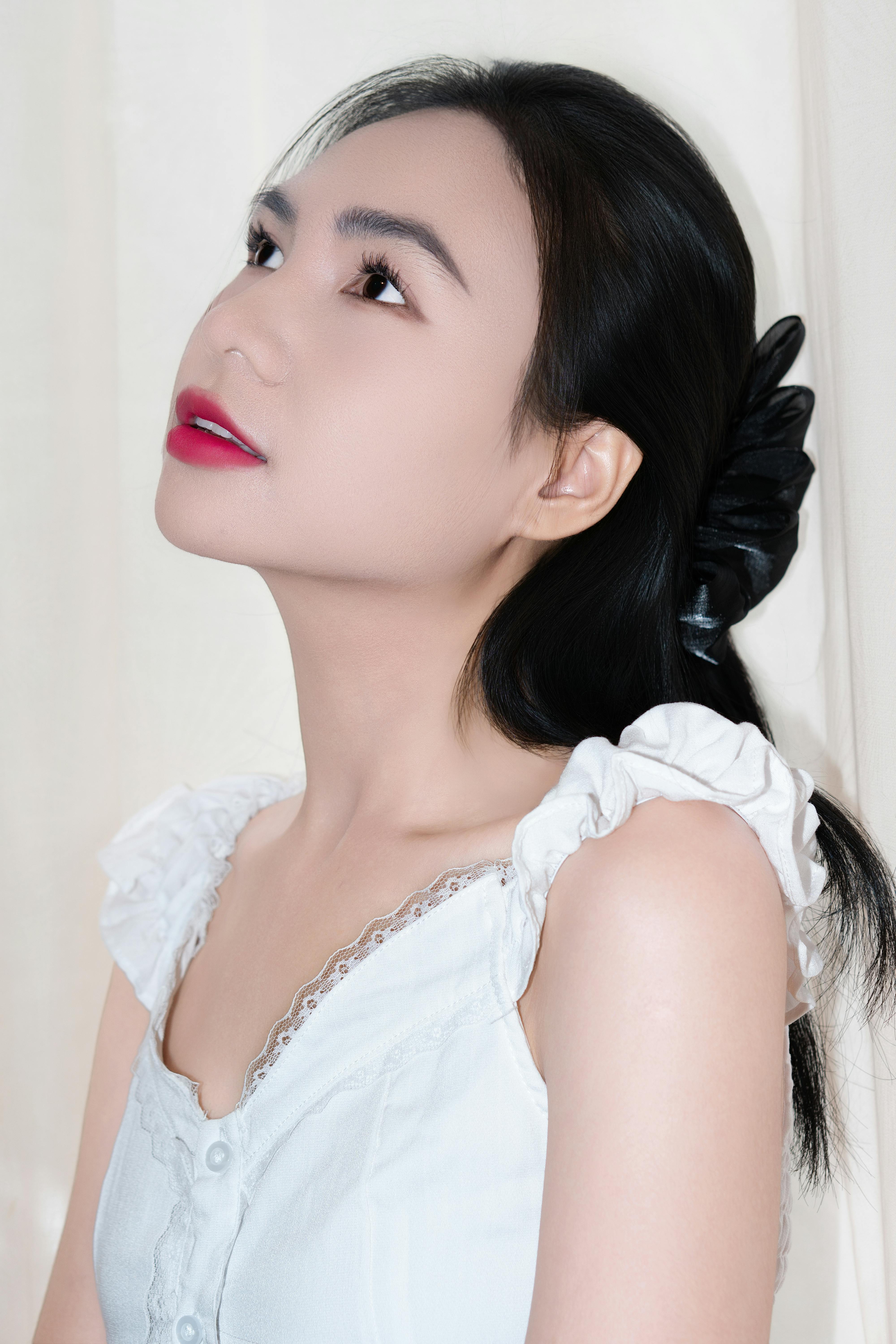 Elegant side profile of a woman with black hair in a white dress, against a neutral background.
