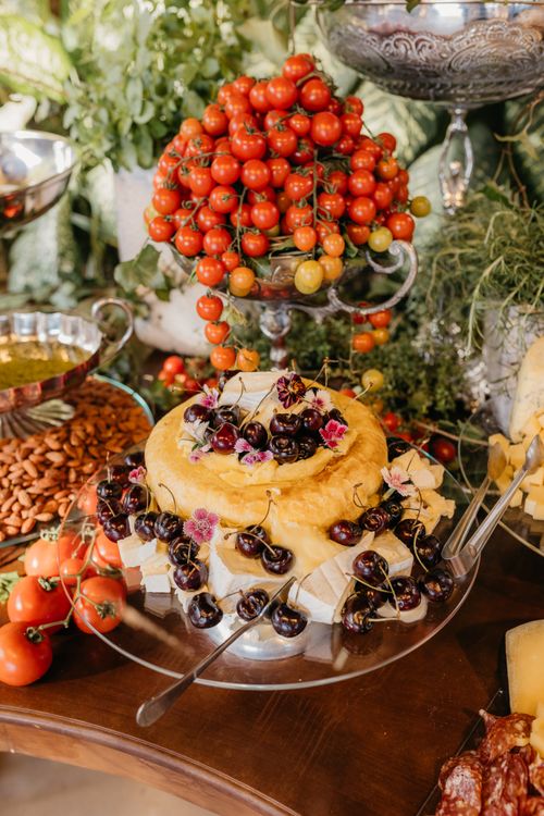 Free A luxurious cheese platter adorned with cherries, tomatoes, and greenery, ideal for gourmet dining. Stock Photo