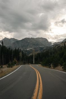 Curved mountain road through a forest with dramatic clouded sky.