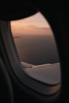 View of endless ocean and coast from airplane window during a serene sunset flight.