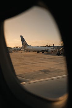 A serene view of an airplane on the tarmac, captured through a window during sunset.
