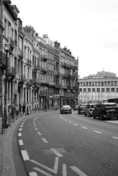 A black and white urban street view in Brussels, Belgium with historic buildings and cars.