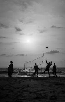 Black and white silhouette of people playing beach volleyball during sunset in India.