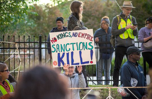 Protesters gather in Towson with signs against sanctions, advocating for peace and justice.