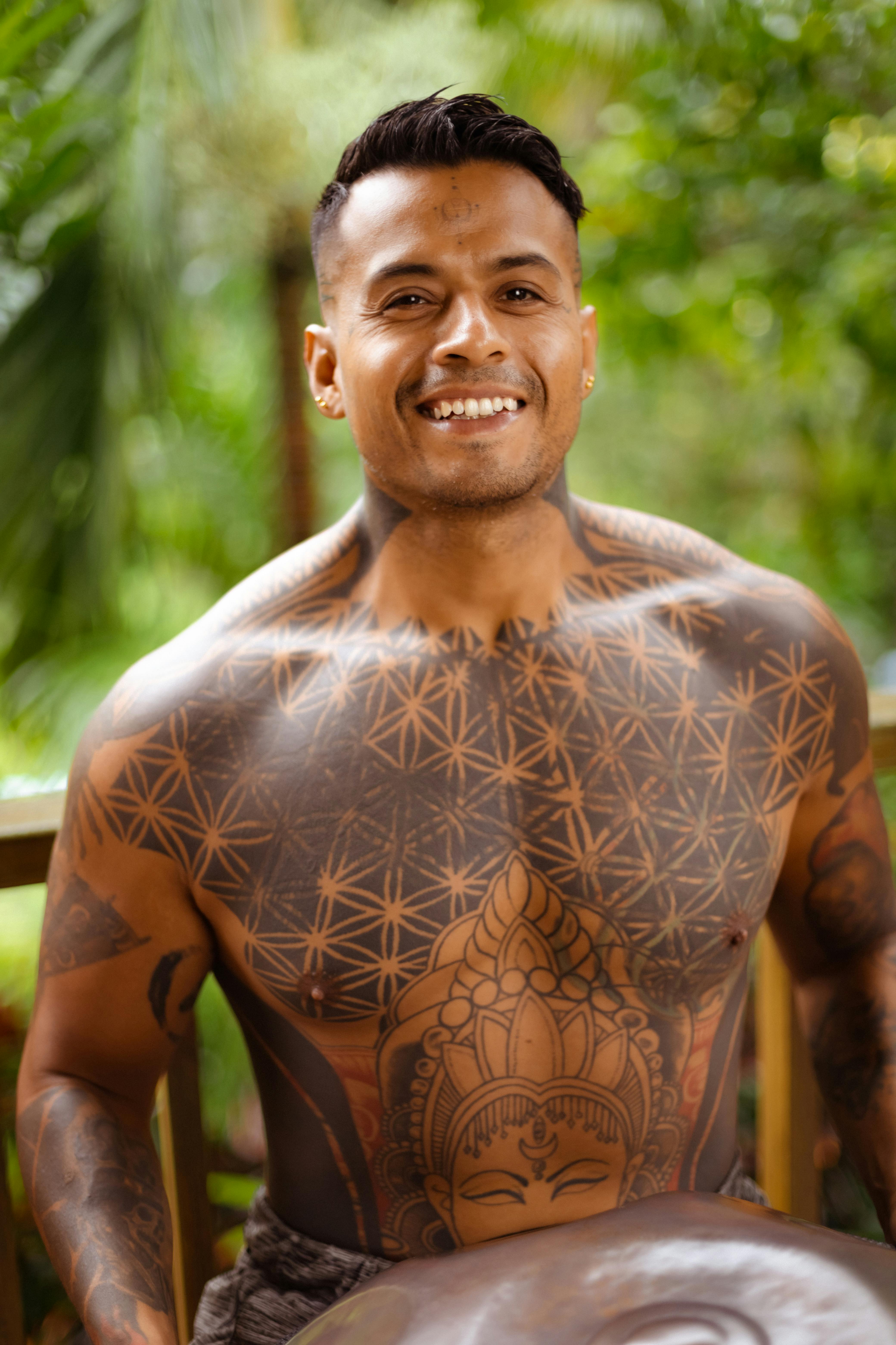 Portrait of a tattooed man smiling outdoors, showcasing intricate designs.