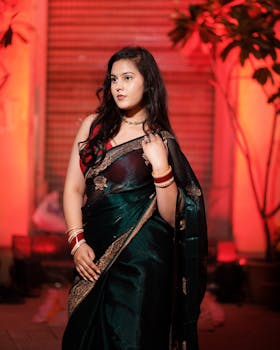 Woman in a stunning green saree with gold accents, set against a warmly lit backdrop.