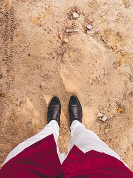 Elegant black shoes and white pants create a minimalist style against a sandy background.