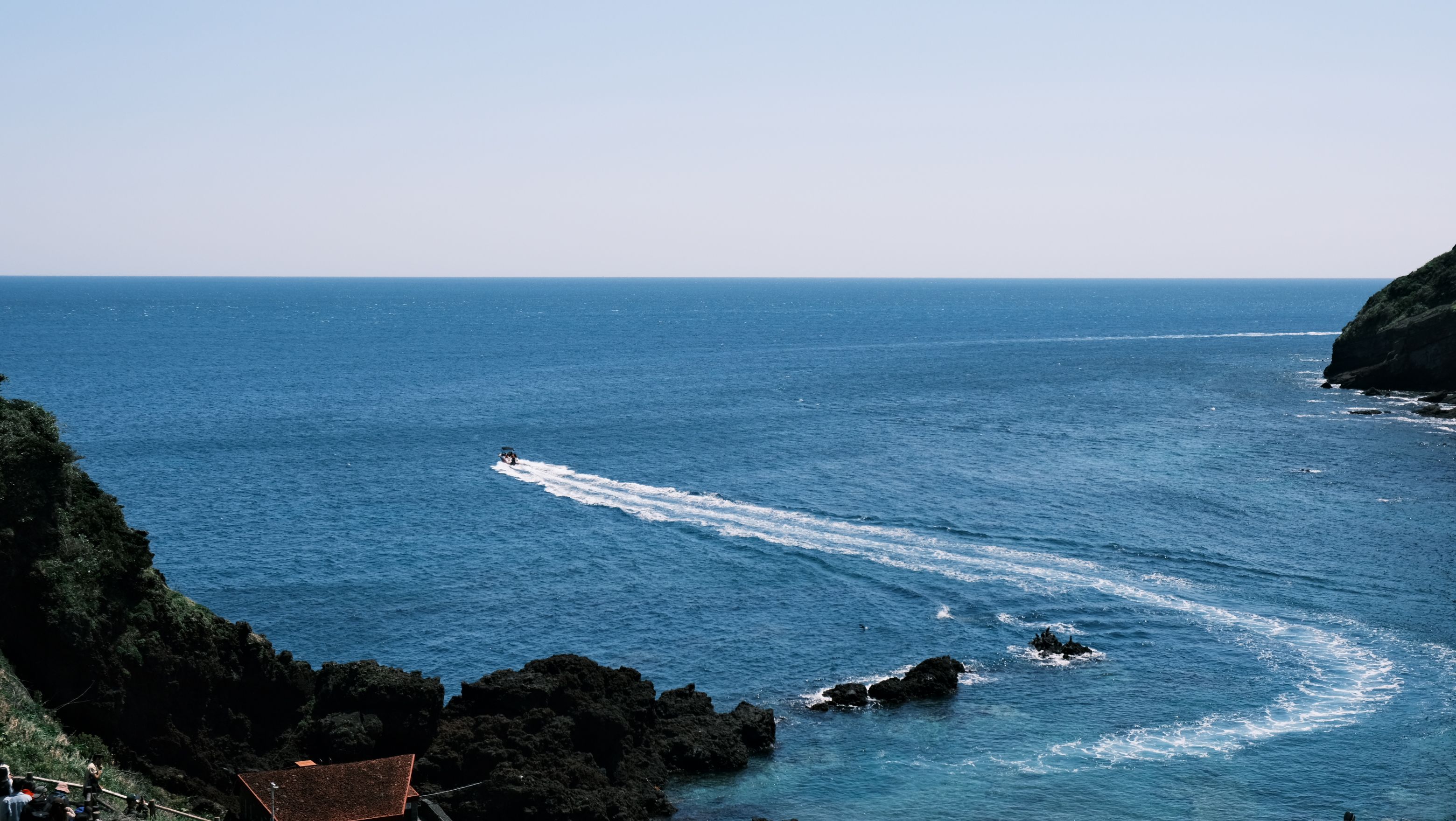 A serene coastal scene featuring a small boat cutting through the blue waters near rocky shores.