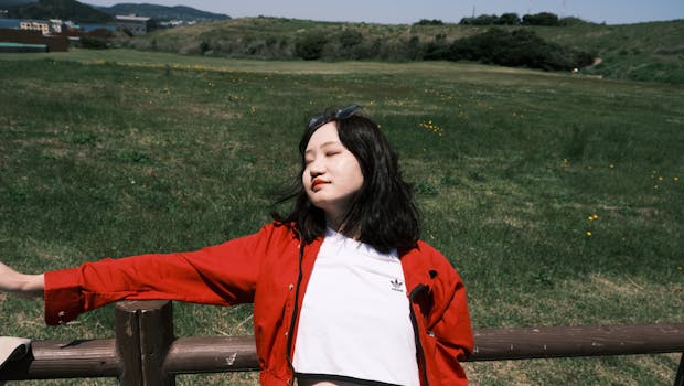 A woman enjoying the sun, leaning against a railing in a lush green outdoor setting.