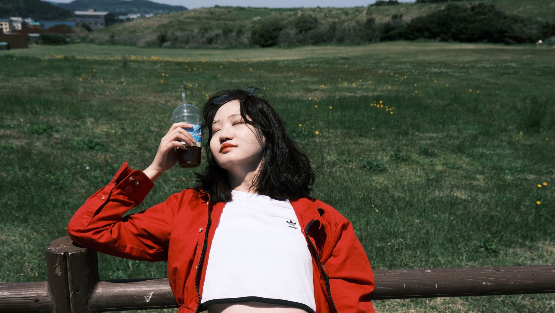 Young woman resting with a drink in a sunny field, enjoying the outdoors.