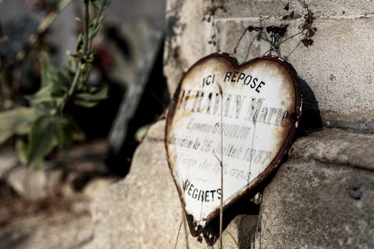 Rustic heart-shaped plaque on a stone wall in Arles cemetery, France.