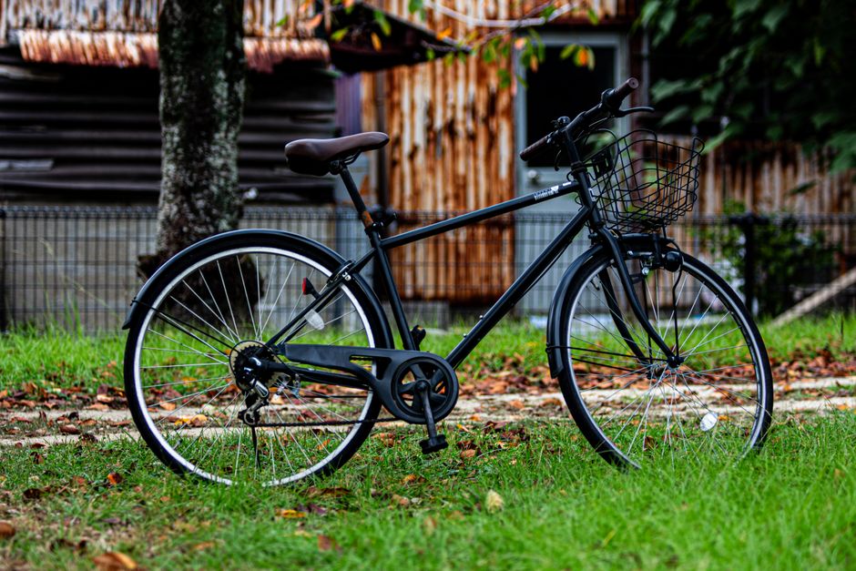 バスケット付きのヴィンテージの黒い自転車が素朴な木造小屋の前の芝生に置かれ、静かな屋外の雰囲気を醸し出しています。