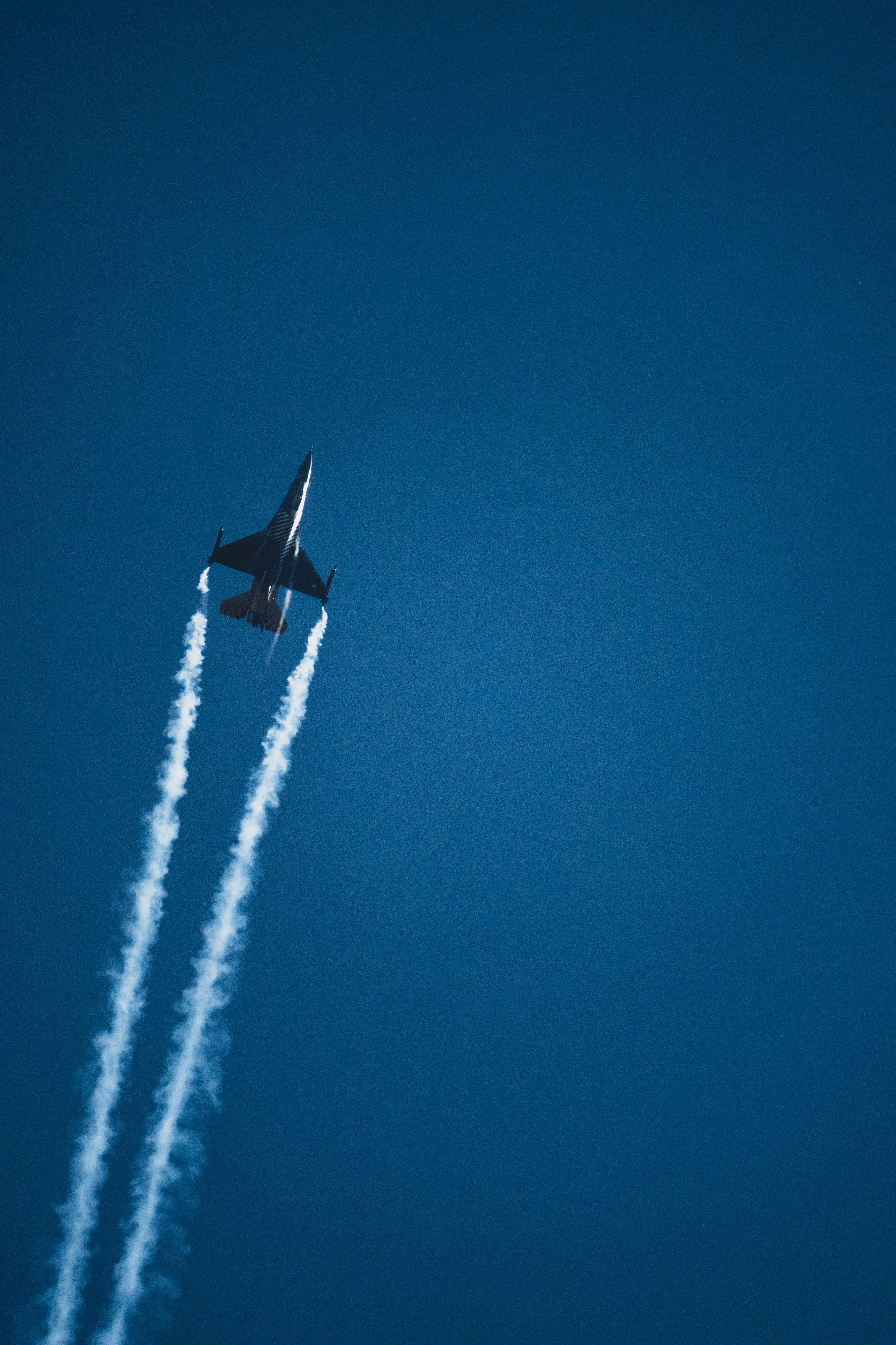 Fighter jet climbing through a deep blue sky with contrails streaming behind it